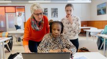 Vrouw aan laptop krijgt hulp van twee vrouwen