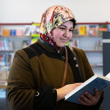 Vrouw met hoofddoek kijkt in boek in bibliotheek