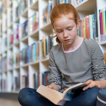 Meisje leest boek in bibliotheek